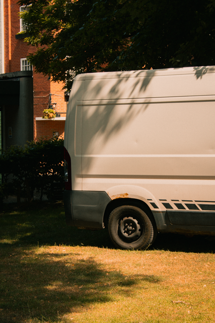 A residential street in Belsize Park with rows of parked cars on both sides of the narrow asphalt road, featuring various models including small hatchbacks and larger vans. The street is lined with te
