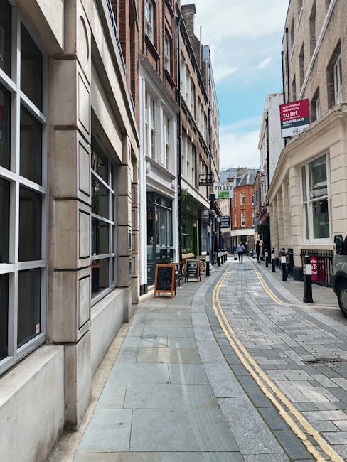 A three-storey brick building with large windows and a bay window at the front, situated on a street corner in Belsize Park. The ground floor features a convenience store with a sign reading 'USMAN SU
